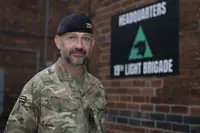 Soldier in camouflage uniform standing in front of a brick wall with a 19th Light Brigade headquarters sign.