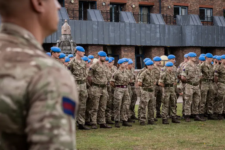 Soldiers in camouflage uniforms with blue berets stand on a parade.