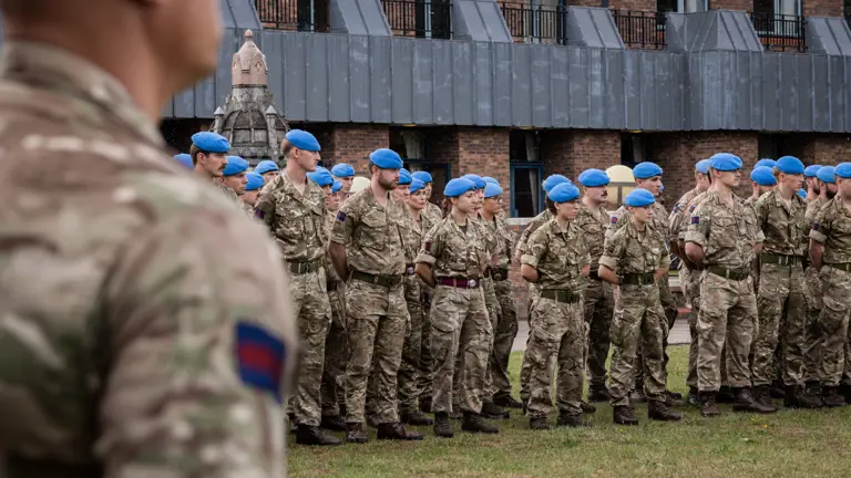 Soldiers in camouflage uniforms with blue berets stand on a parade.