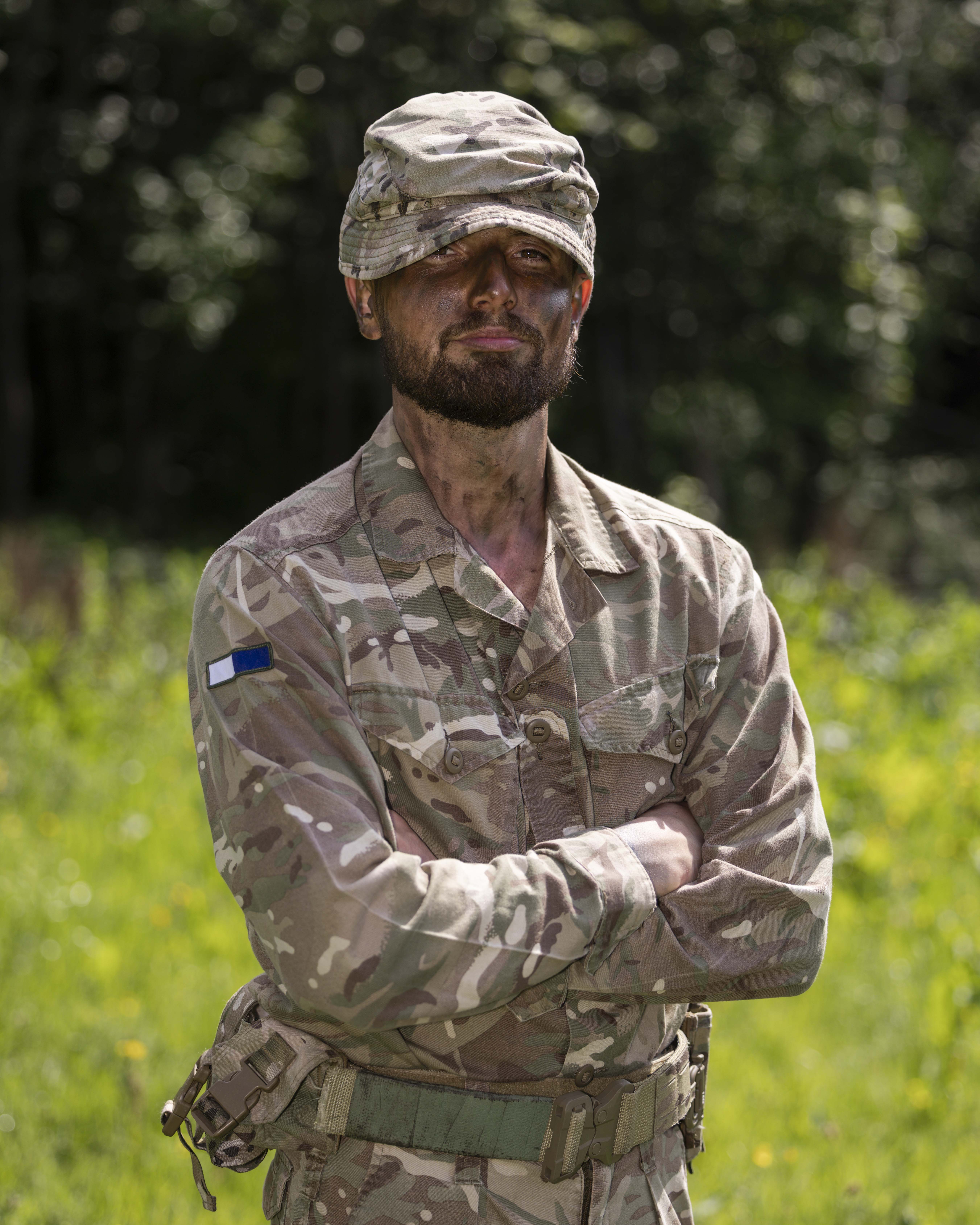 Portrait of soldier in camouflage uniform and hat with a green grassy background.