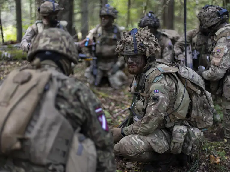 Group of soldiers in camouflage gear gathered in a forest clearing during a tactical exercise.