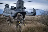 Two soldiers in camouflage uniform are seen running out the back of a Chinook with rifles and army gear into a field.