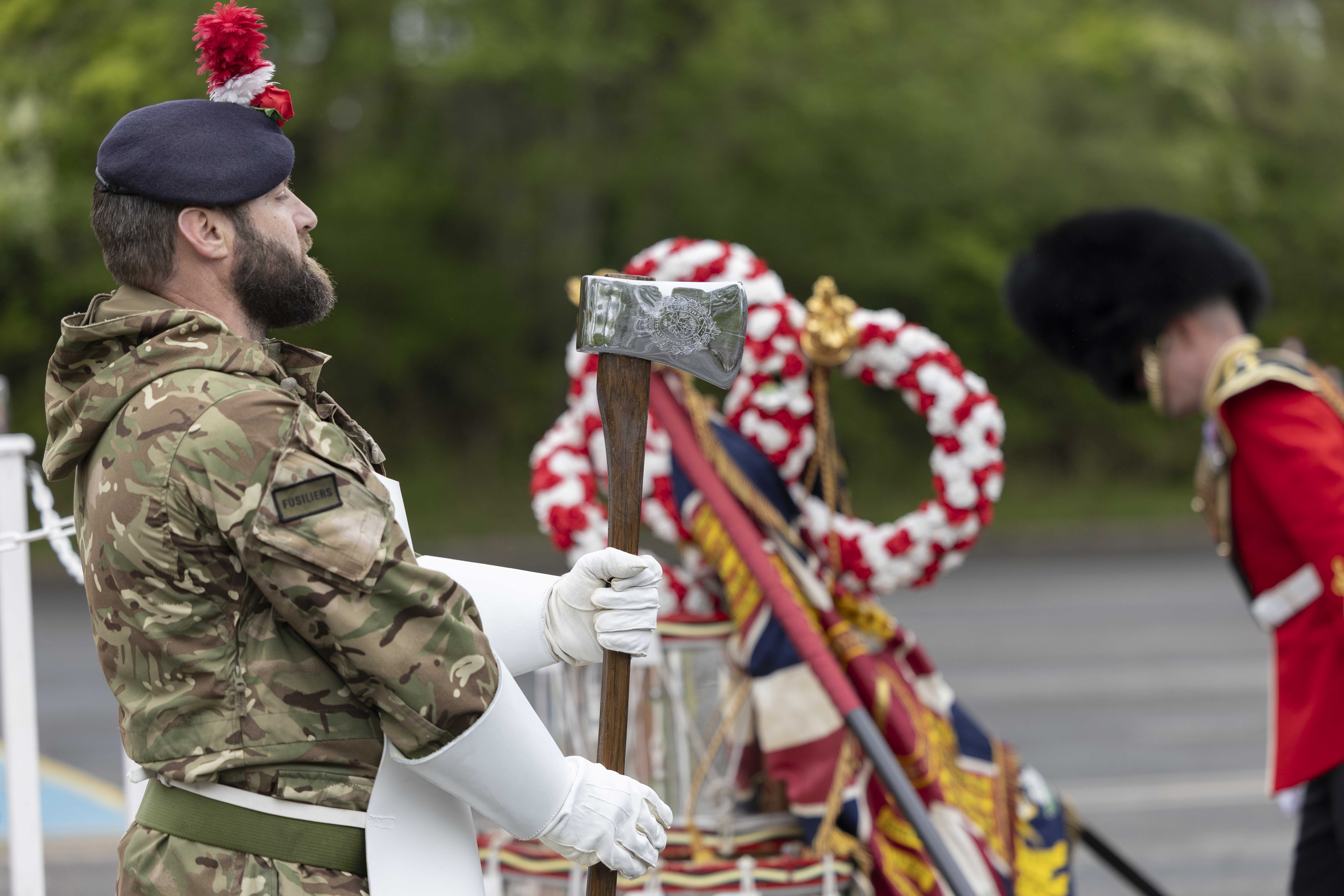 A soldier holding an axe and wearing a white apron stands in front of ceremonial drums.