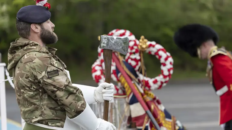 A soldier holding an axe and wearing a white apron stands in front of ceremonial drums.