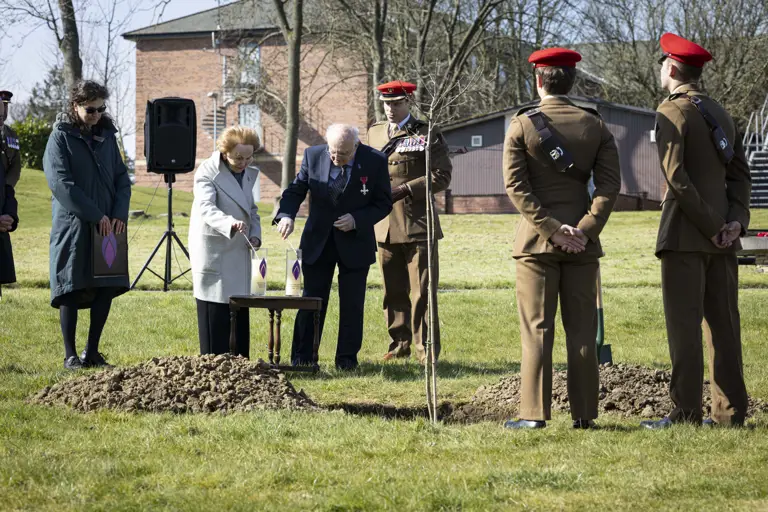 Holocaust survivors Mala Tribich MBE and Dr Alfred Garwood MBE light Holocaust candles on an army camp during a memorial service. Surrounded by several soldiers in their number 2 uniforms.