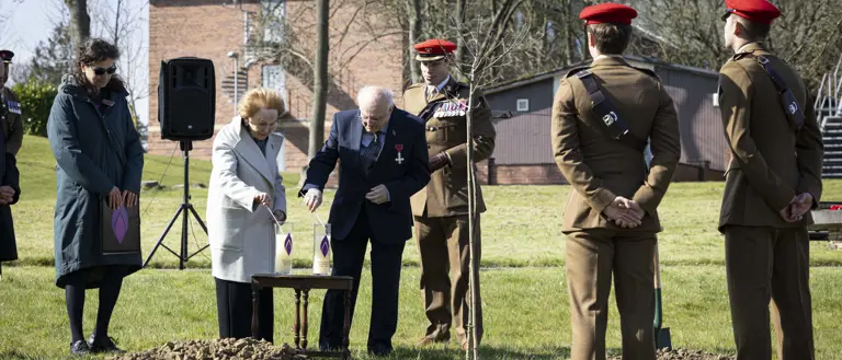 Holocaust survivors Mala Tribich MBE and Dr Alfred Garwood MBE light Holocaust candles on an army camp during a memorial service. Surrounded by several soldiers in their number 2 uniforms.