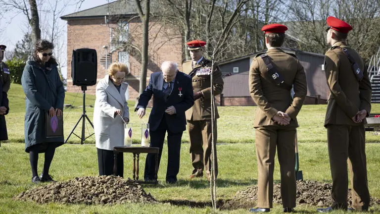 Holocaust survivors Mala Tribich MBE and Dr Alfred Garwood MBE light Holocaust candles on an army camp during a memorial service. Surrounded by several soldiers in their number 2 uniforms.