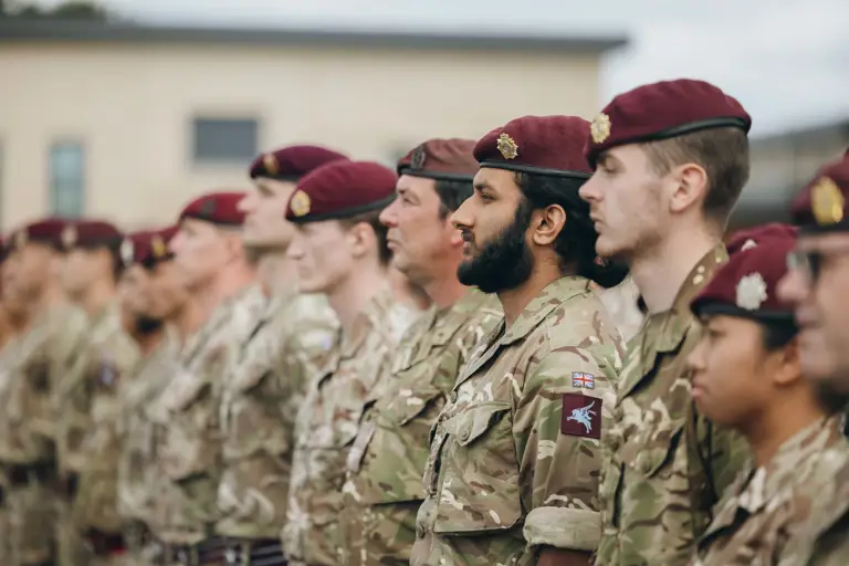 Soldiers wearing camouflage uniforms and maroon berets stand on a parade.