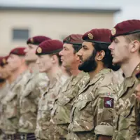Soldiers wearing camouflage uniforms and maroon berets stand on a parade.
