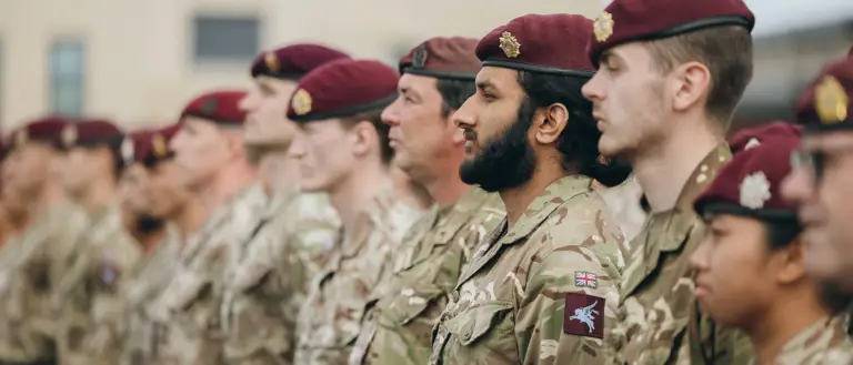 Soldiers wearing camouflage uniforms and maroon berets stand on a parade.