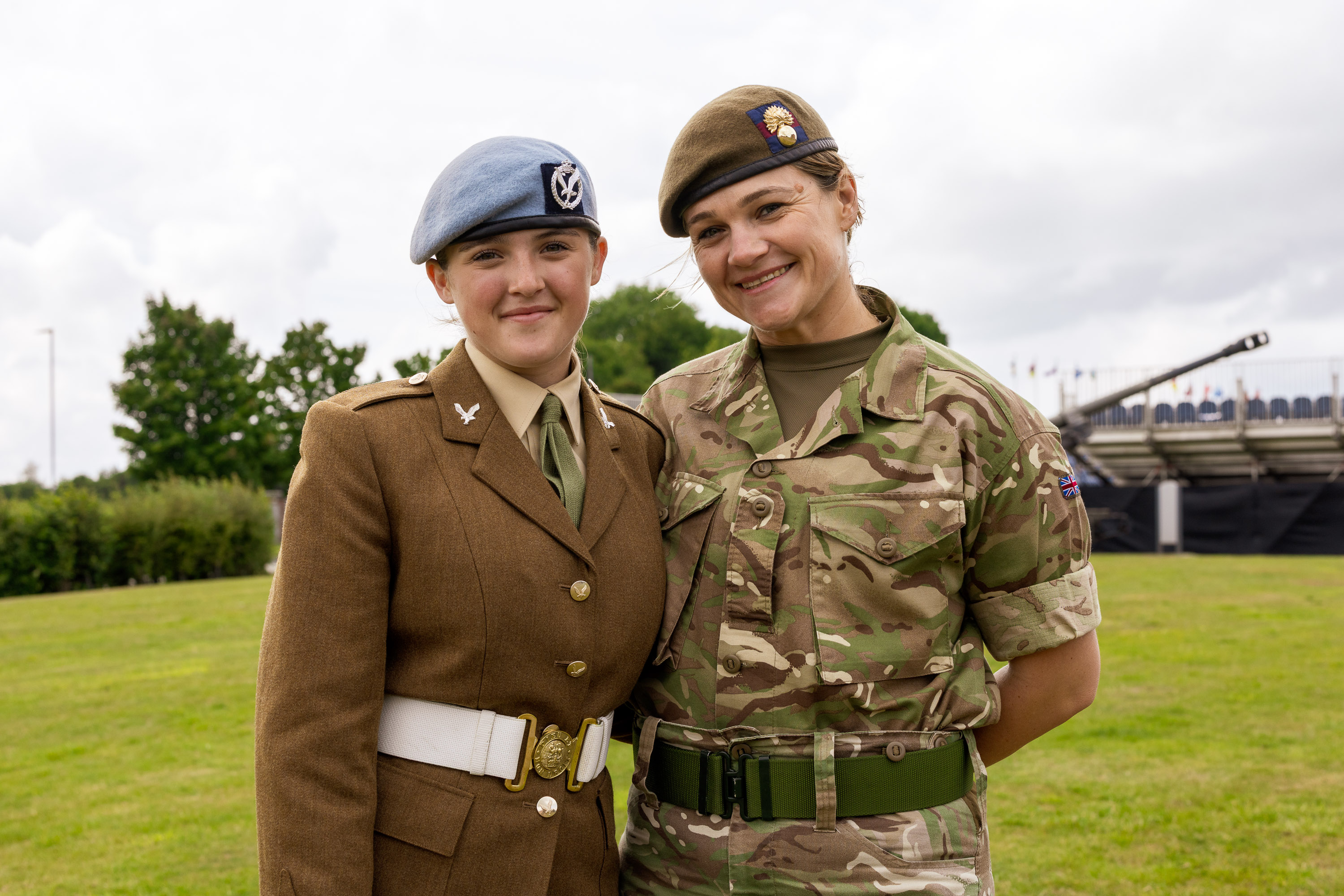 Chloe is photographed in her brown uniform and blue Army Air Corps beret stood next to her mum Sherene who is dressed in her camouflage uniform. They are both smiling and have their arms around each others back.  