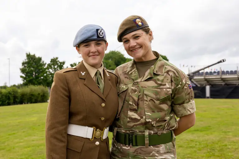 Chloe is photographed in her brown uniform and blue Army Air Corps beret stood next to her mum Sherene who is dressed in her camouflage uniform. They are both smiling and have their arms around each others back.