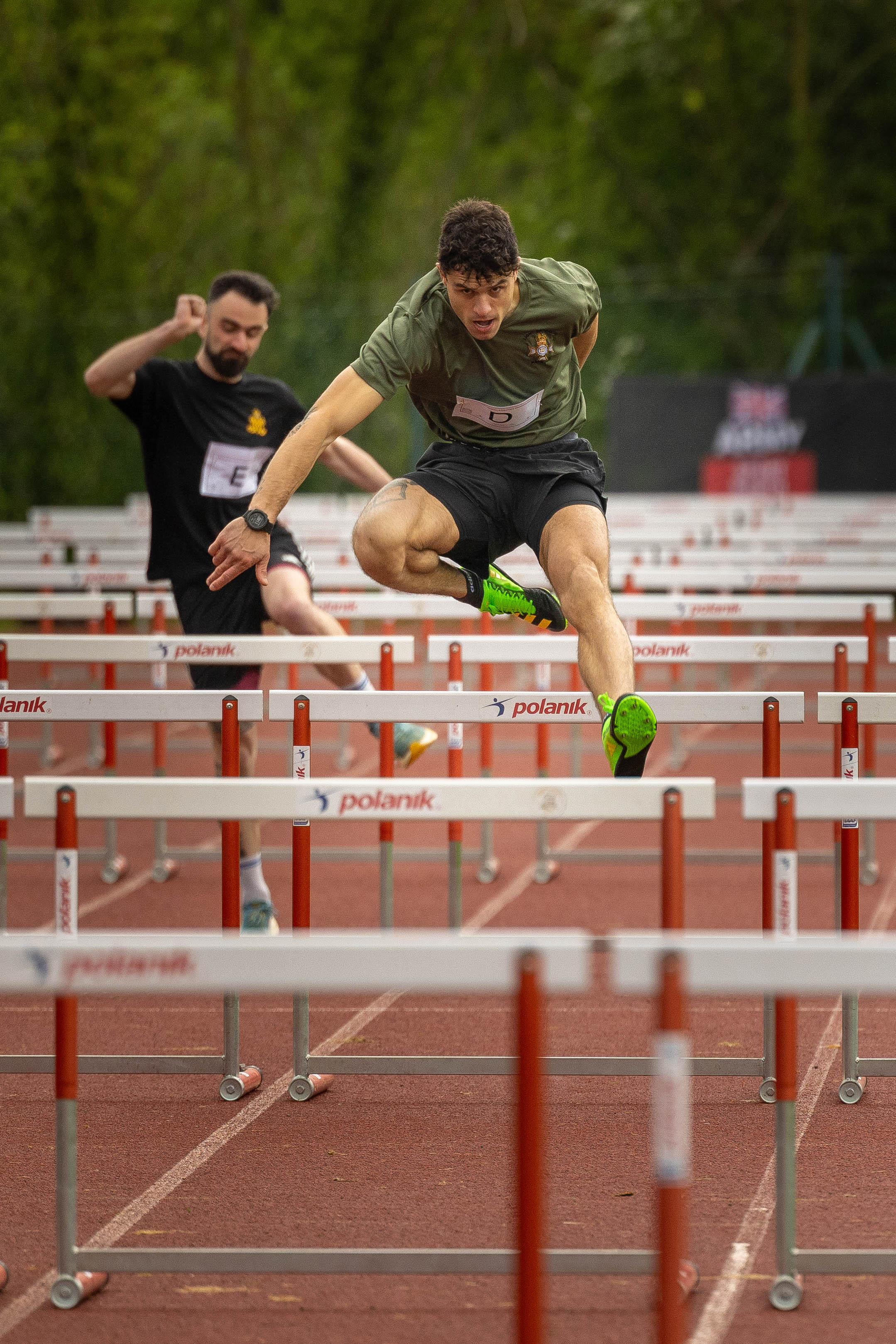 Two people are competing in a track and field hurdle race. The focus is on one participant in the foreground.