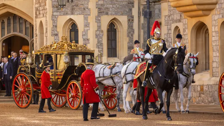 Ornate carriage with golden details, pulled by four white horses, escorted by guards in red uniforms and a knight. Historic castle backdrop. Regal ambiance.