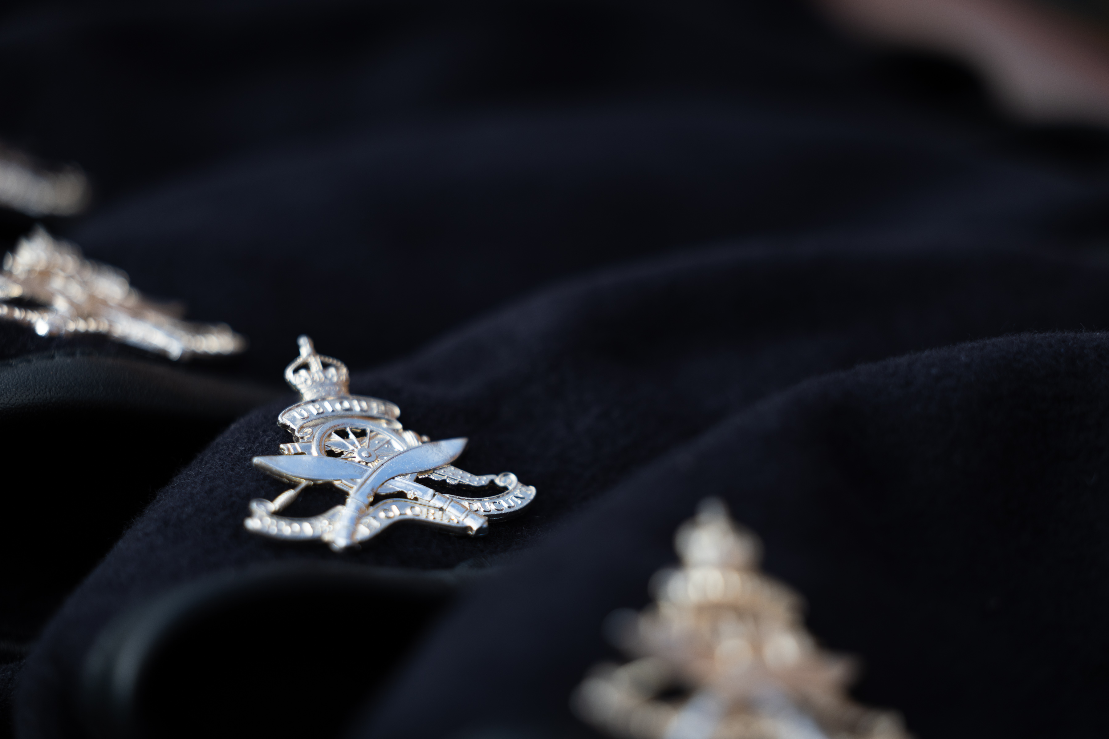 Three dark blue berets are lying in a line on a table featuring a British Army unit cap badge.