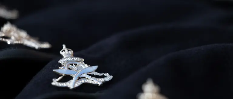 Three dark blue berets are lying in a line on a table featuring a British Army unit cap badge.