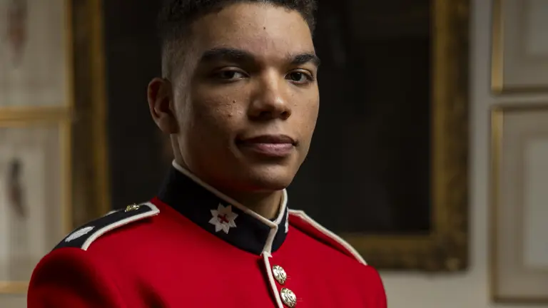 A soldier in a red tunic holds out several medals.