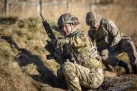Two soldiers in uniform are pictured during a training exercise, the man closest is holding a gun and pointing.