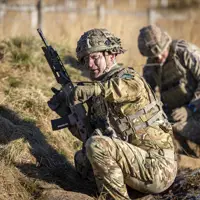 Two soldiers in uniform are pictured during a training exercise, the man closest is holding a gun and pointing.