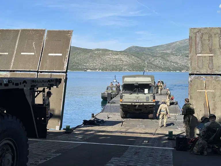 A green military truck drives from a military ferry.