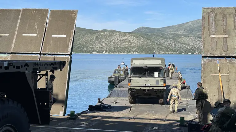 A green military truck drives from a military ferry.