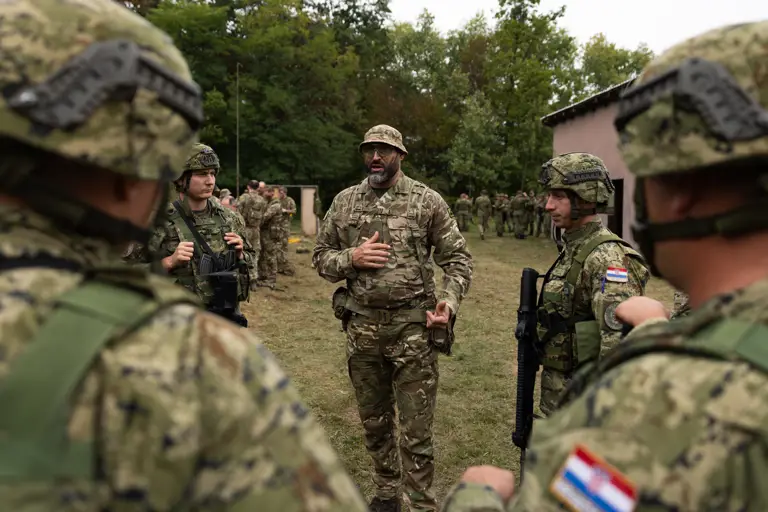 soldiers from both the British Army and the Croatian Armed Forces stand talking outside a building on exercise wearing their different camouflage uniforms