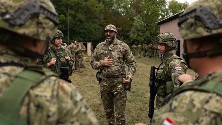 soldiers from both the British Army and the Croatian Armed Forces stand talking outside a building on exercise wearing their different camouflage uniforms