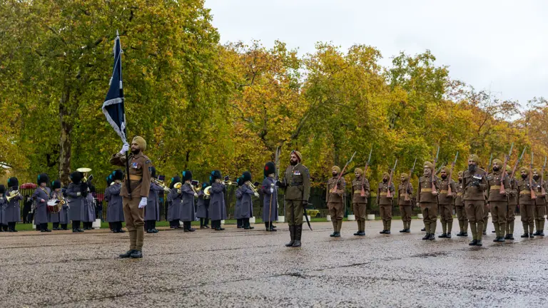 Soldiers in brown uniforms and turbans stand in formation during a ceremonial parade with a band in the background.