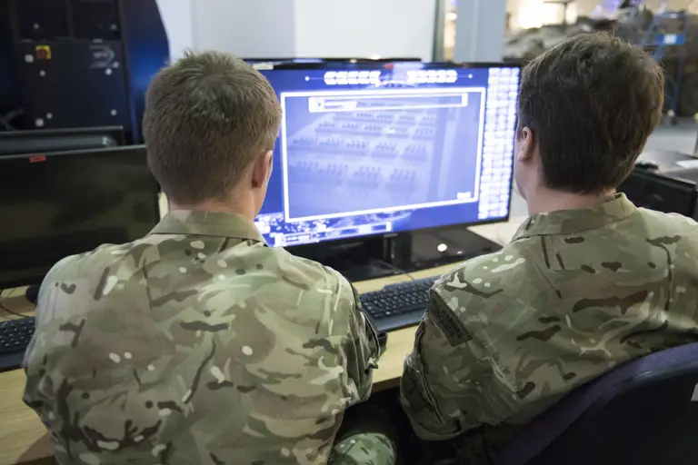 Two soldiers in camouflage uniforms analyzing tactical data on a computer screen.