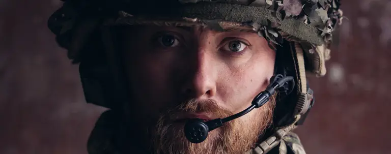 A close up of a soldier in uniform, his helmet and a microphone are visible.