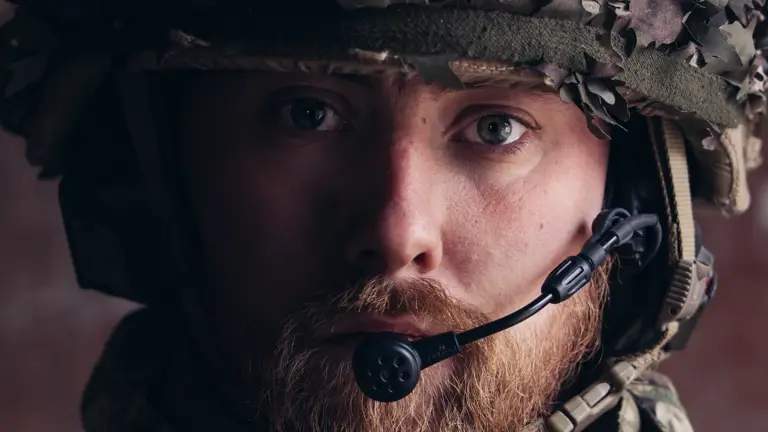 A close up of a soldier in uniform, his helmet and a microphone are visible.