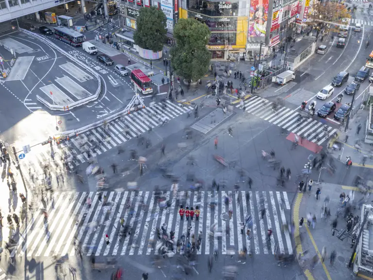 A bird's eye view shot of four soldiers in red tunics and bearskin hats on a crossing in Tokyo, pedestrians are a blur around them.