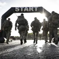 Six soldiers in full camouflage gear approach a start line during a training exercise.