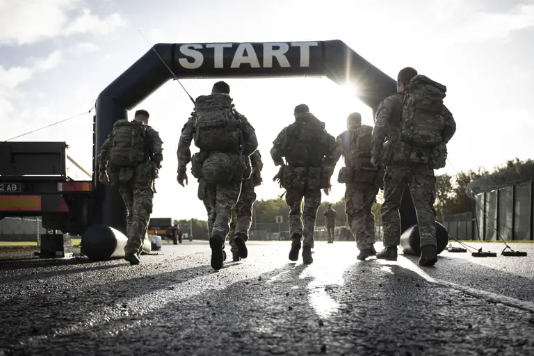 Six soldiers in full camouflage gear approach a start line during a training exercise.