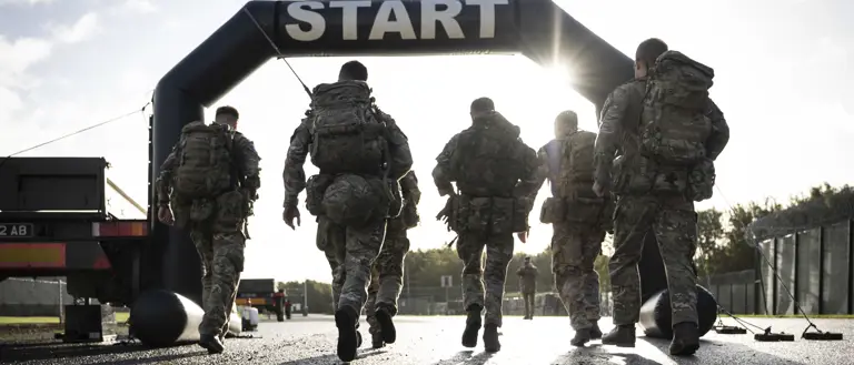 Six soldiers in full camouflage gear approach a start line during a training exercise.
