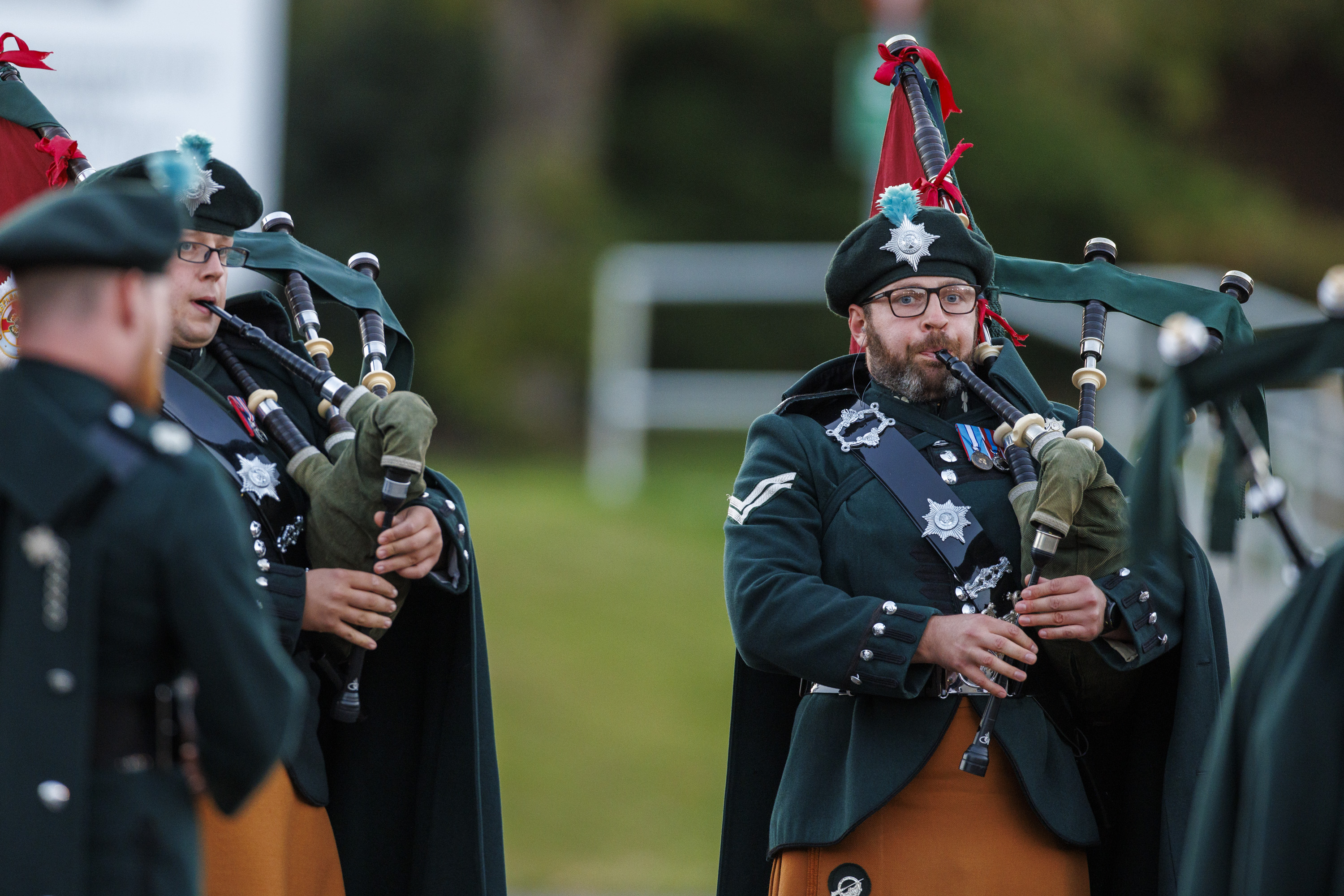 A bagpiper in a green and orange ceremonial uniform playing a bagpipe. 