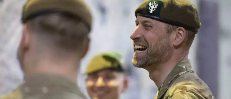 Three individuals in military uniforms are standing together, smiling.