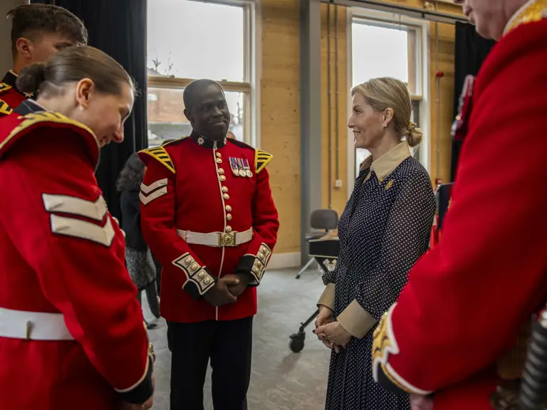 Her Royal Highness, The Duchess of Edinburgh, stands talking to soldiers wearing red tunics.