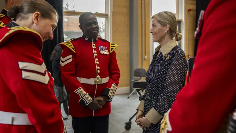 Her Royal Highness, The Duchess of Edinburgh, stands talking to soldiers wearing red tunics.