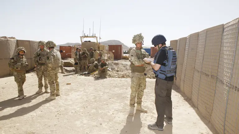 Soldier Magazine journalist wearing a helmet and bullet proof vest in Afghanistan in seen writing into a notebook while interviewing a soldier.