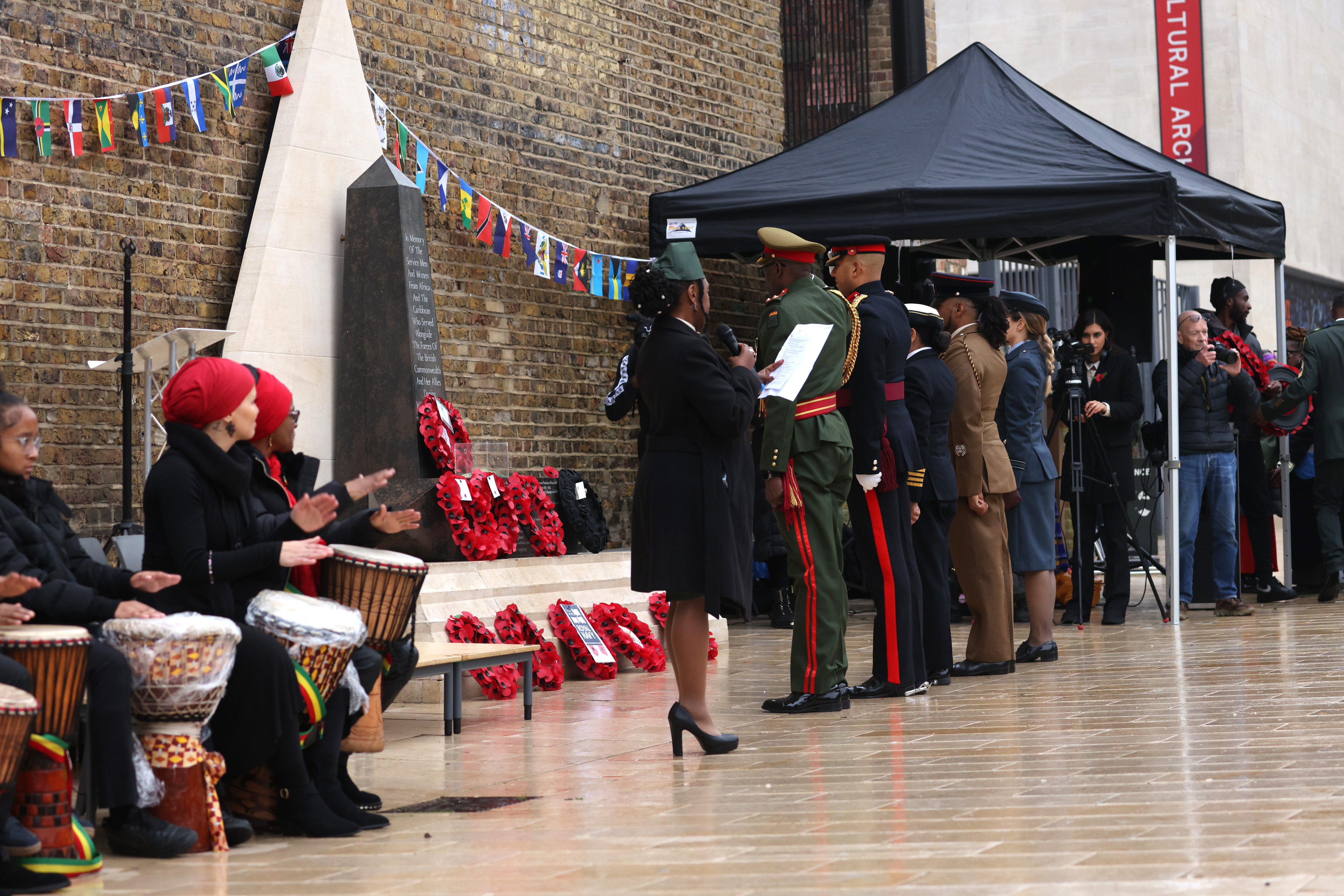 Soldiers, sailors and airmen stand in ceremonial uniforms in front of a memorial.