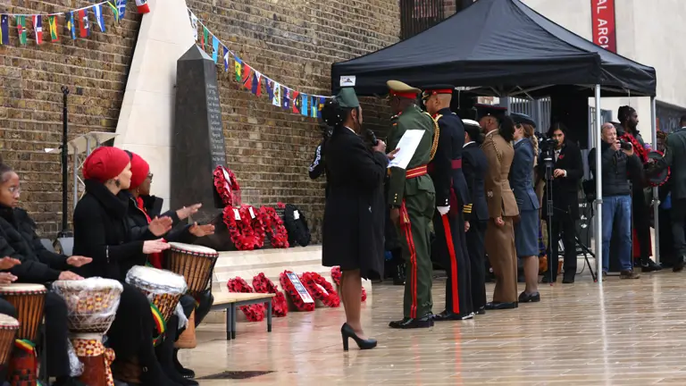 Soldiers, sailors and airmen stand in ceremonial uniforms in front of a memorial.