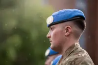 A soldier stands with a blue beret on his head.