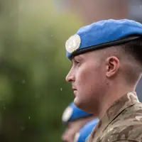 A soldier stands with a blue beret on his head.