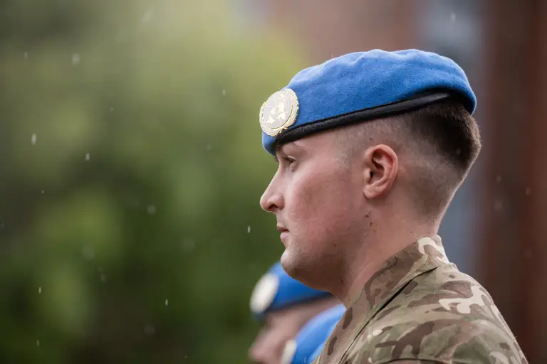 A soldier stands with a blue beret on his head.