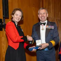 Military personnel in formal attire shake hands as an award is exchanged.