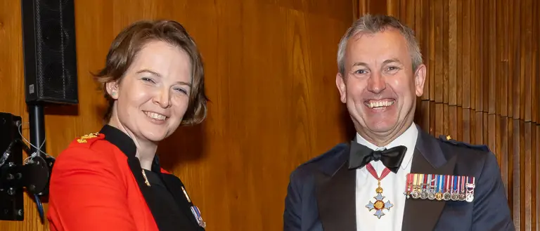 Military personnel in formal attire shake hands as an award is exchanged.