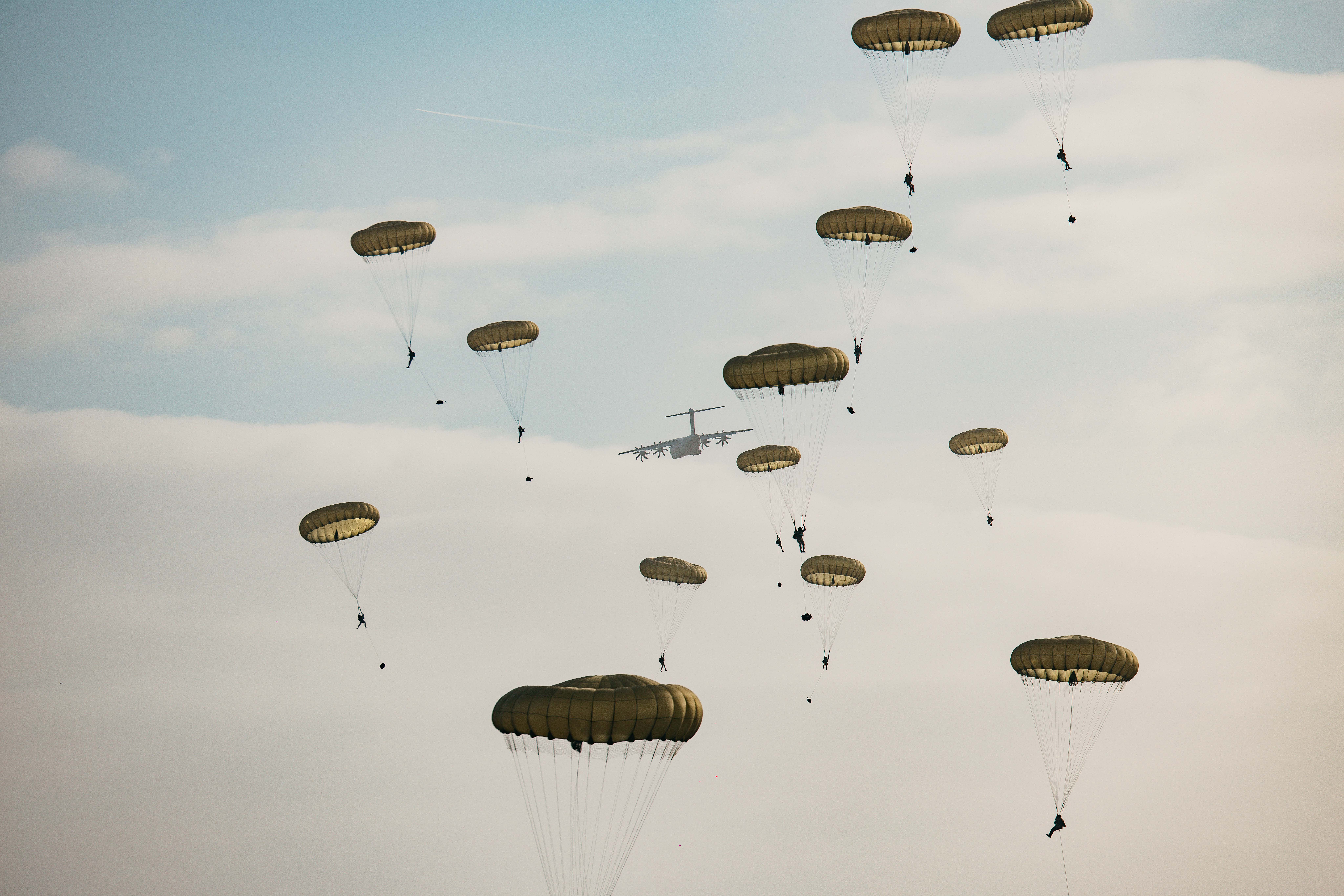 Multiple parachutes with individuals descending from a military aircraft in the sky.