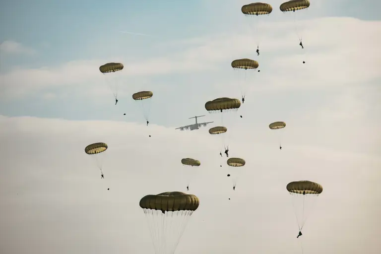 Multiple parachutes with individuals descending from a military aircraft in the sky.
