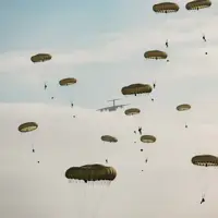 Multiple parachutes with individuals descending from a military aircraft in the sky.